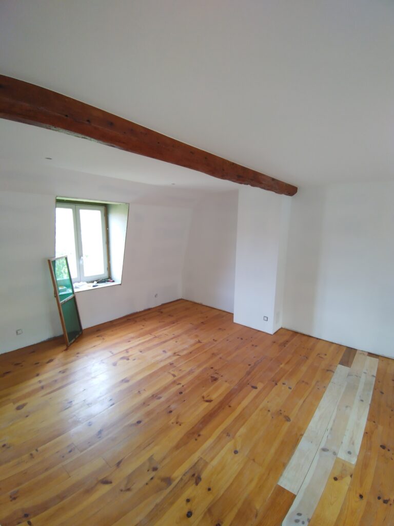 Agencement intérieur : pièce rénovée avec parquet bois, murs blancs et poutre apparente.