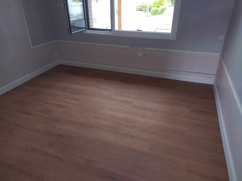 Agencement intérieur : pose de parquet stratifié bois dans une pièce rénovée, finition soignée au pied du mur.