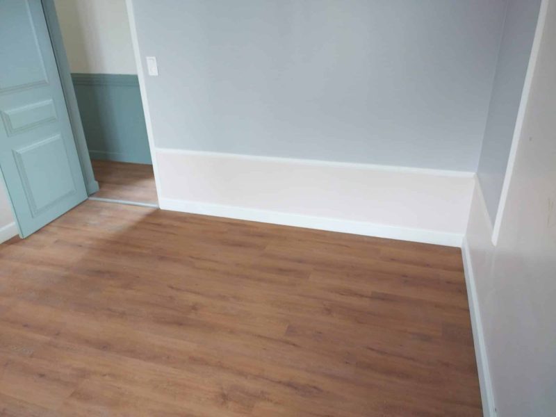 Agencement intérieur : pose de parquet stratifié bois dans une pièce rénovée, finition soignée au pied du mur.