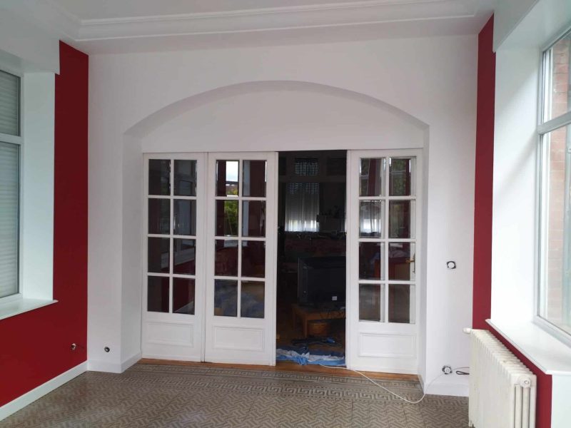 Agencement intérieur : portes vitrées blanches sous arche, murs rouges et finition soignée par Dupuis & Associés.